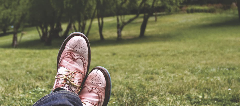 Entspannt verschränkte Füße in einem Paar Herrenschuhen aus Leder in Parklandschaft, als Synonym für eine erfolgreiche Schuldenbereingung Privatinsolvenz Itzehoe