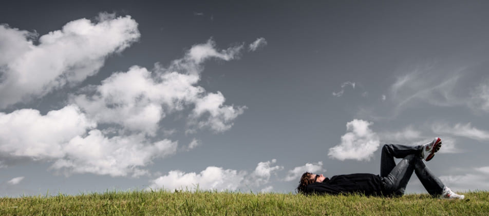 Junger Mann entspannt auf dem Rücken liegend in der Sonne auf dem Rasen nach erfolgreicher Hilfe zur Schuldenbereingung Privatinsolvenz Kiel